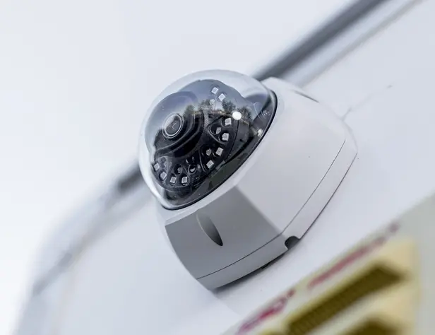 Dome security camera mounted on a white wall angled downward for vigilance and capturing surveillance footage.