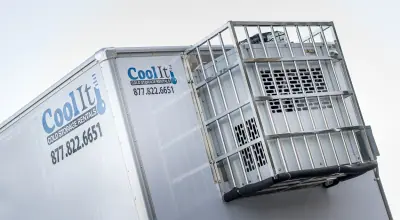 Cool It refrigerated truck with a cooling unit in a metal cage, displaying a phone number against a clear sky.