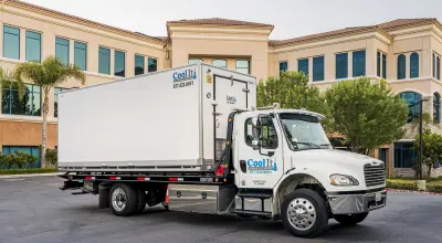 Coolife white refrigerated delivery truck parked in front of a beige office building lined with palm trees.