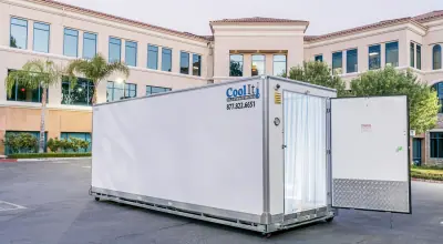White refrigerated container with the door open in a sunny courtyard with an office building and palm trees.