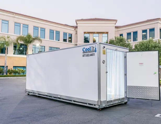 White refrigerated container with the door open in a sunny courtyard with an office building and palm trees.